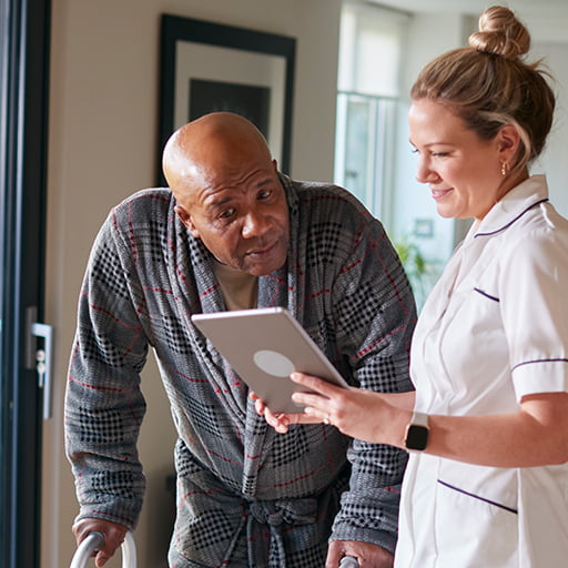 elderly man with walker looking at a tablet held by a nurse