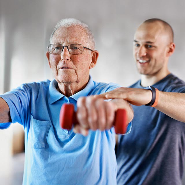 Senior man exercising with staff member in senior living community