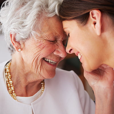 senior living community resident smiling and touching foreheads with daughter