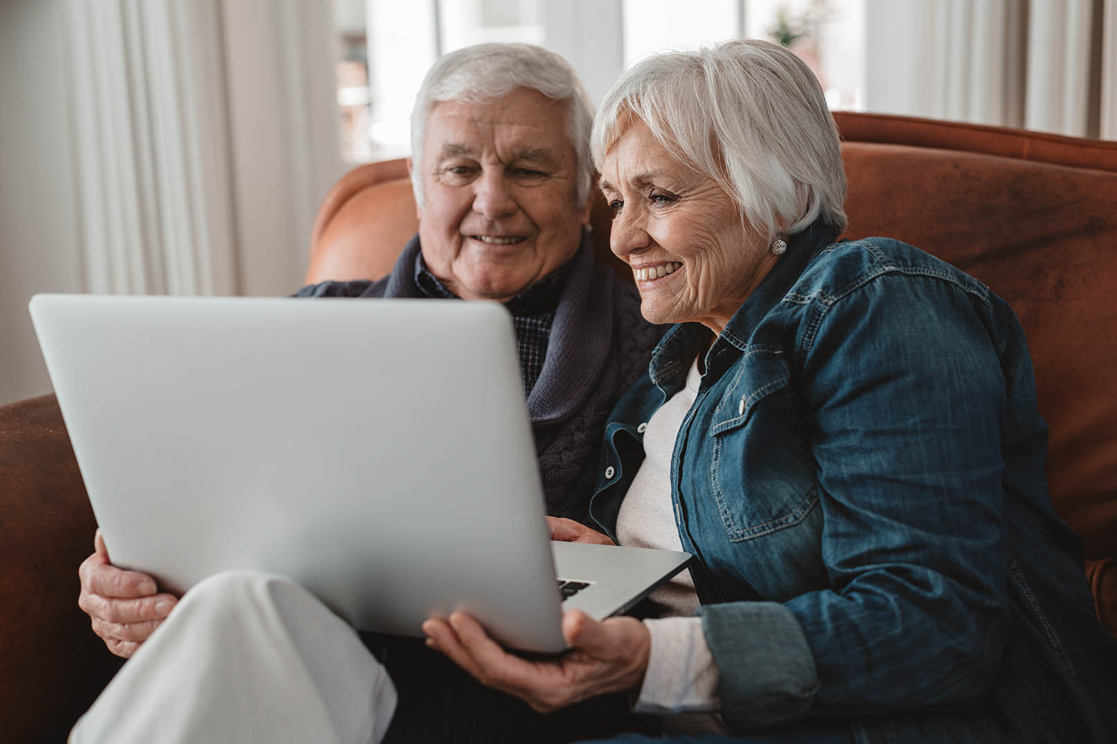 Smiling senior couple using a laptop on their sofa to find Memory Care options