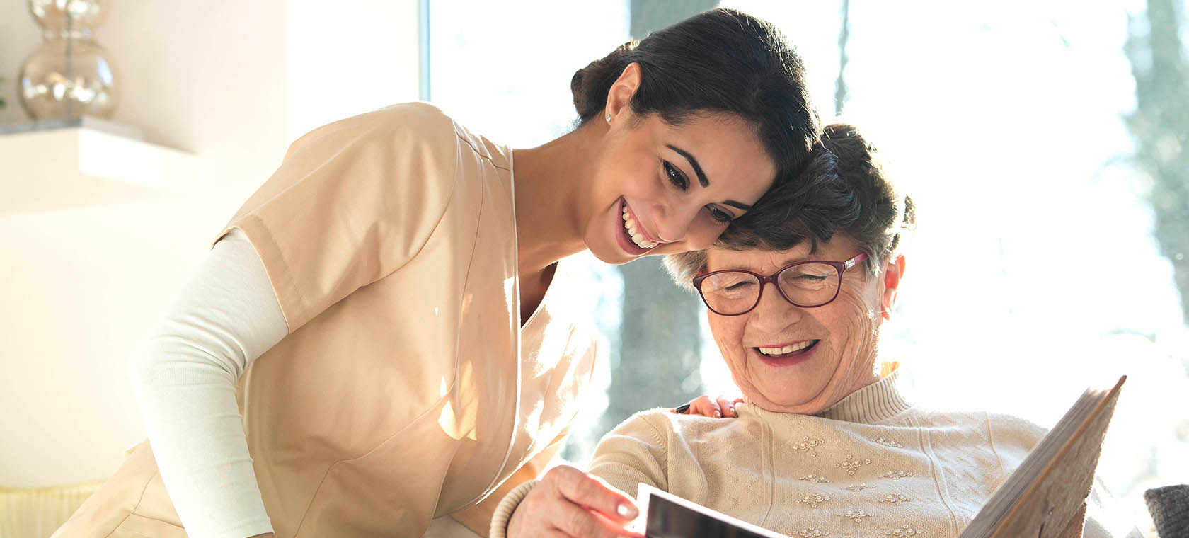 Senior woman with Alzheimer's looking at photo album with nurse