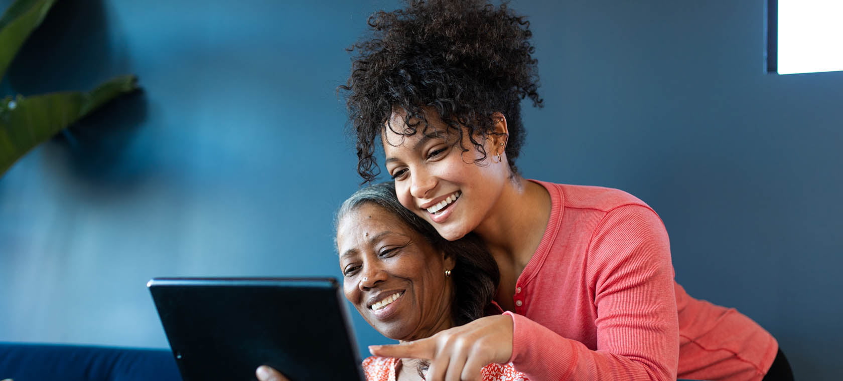 Senior woman with adult child over her shoulder looking at a tablet and smiling